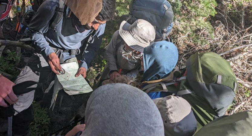 A group of people wearing backpacks stand in a circle and examine a map.